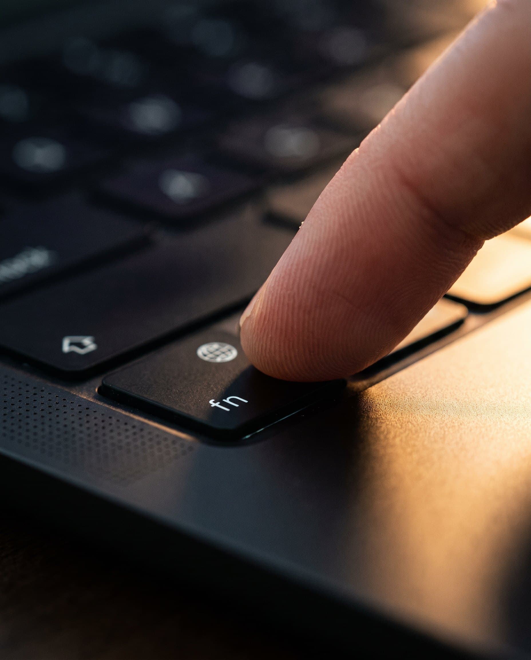 A fingertip holding the fn key on a Space Black MacBook keyboard