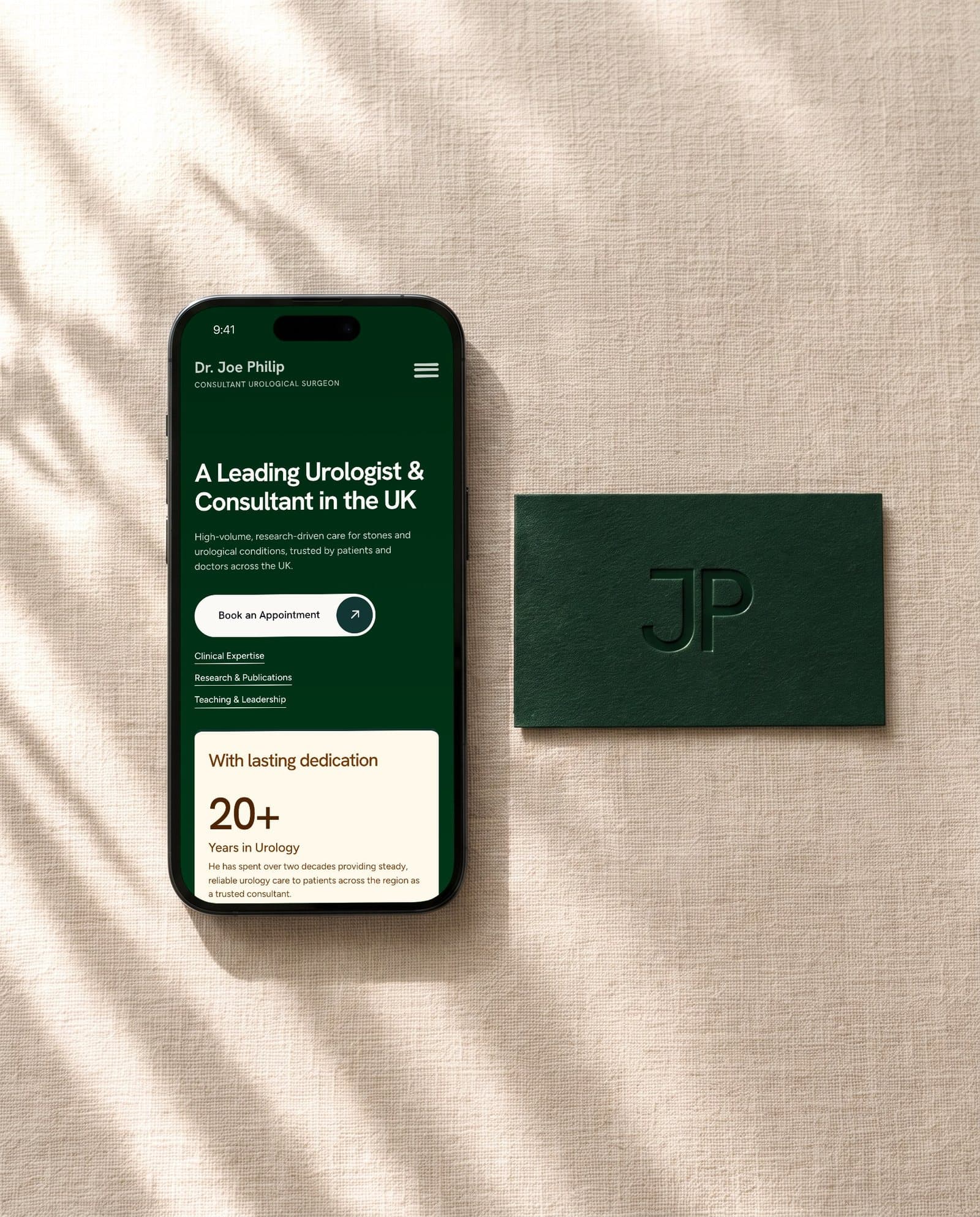 An iPhone lying straight on cream linen beside the debossed JP card, Joe Philip's mobile site on screen